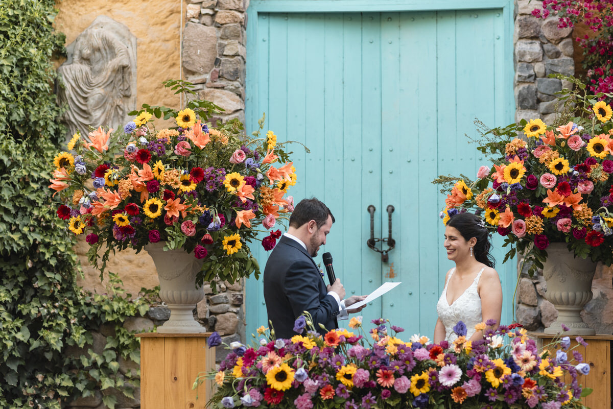 Nacho leyendo los votos a Nacha - Nacho & Nacha - Matrimonio en Casa Olivos de Chacabuco - Altar de matrimonio con flores muy coloridas. Nacho y Nacha sonriendo.
